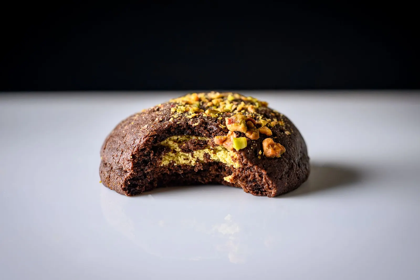A chocolate cookie with a bite taken out showing a green pistachio filling